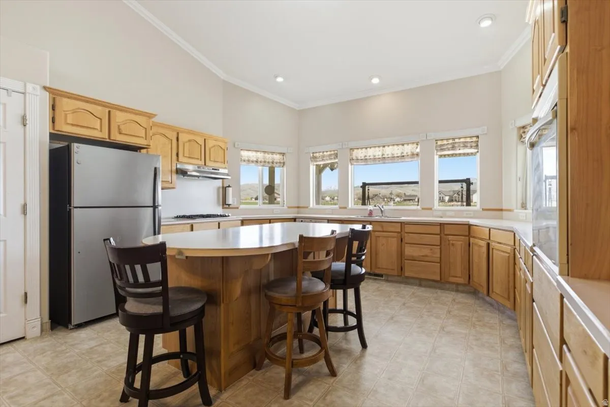 Kitchen with light countertops, a breakfast bar area, freestanding refrigerator, ornamental molding, and a center island