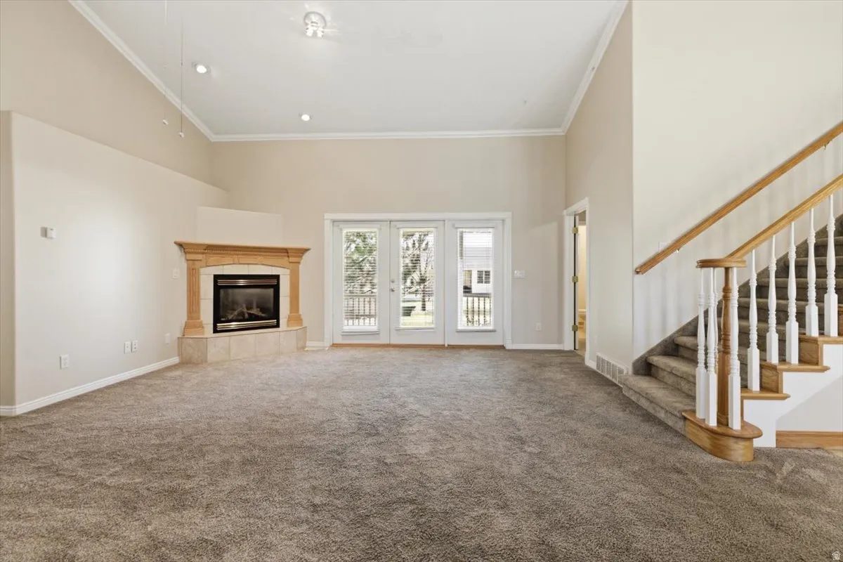 Unfurnished living room featuring a high ceiling, carpet flooring, ornamental molding, and a tile fireplace