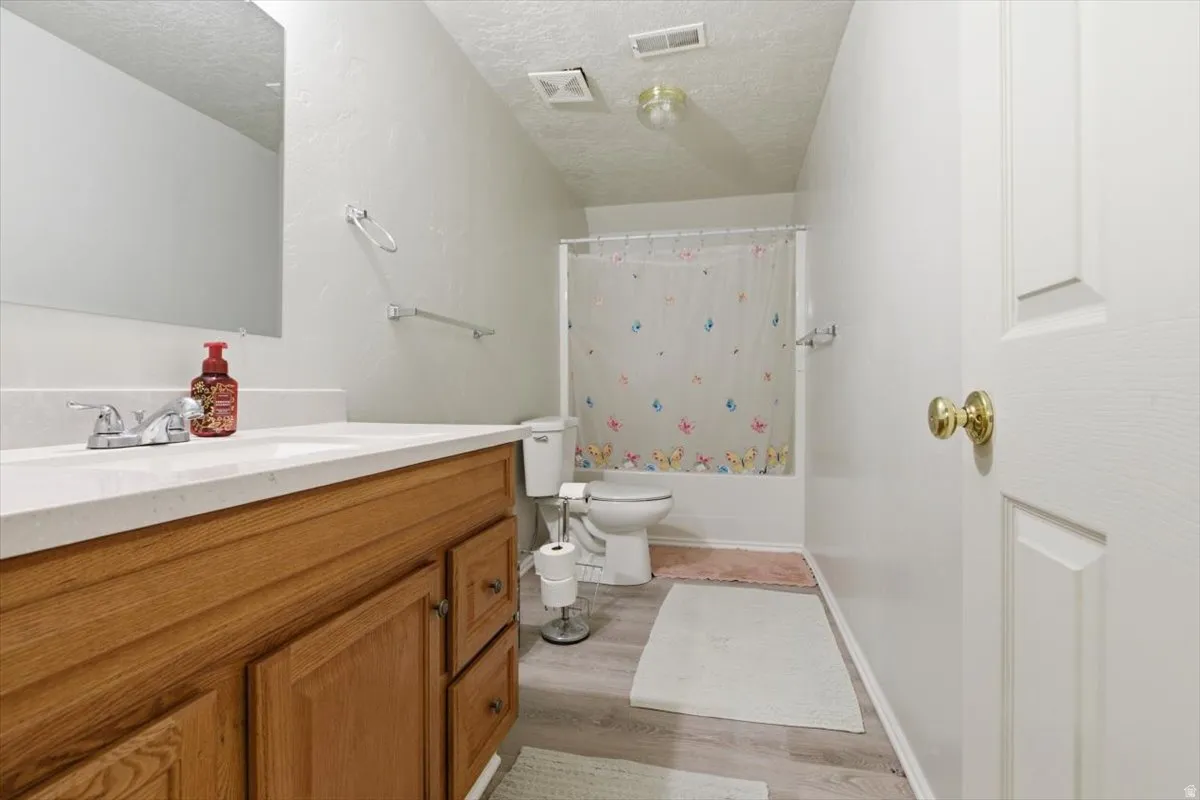 Full bath with vanity, shower / bath combo, light wood finished floors, and a textured ceiling