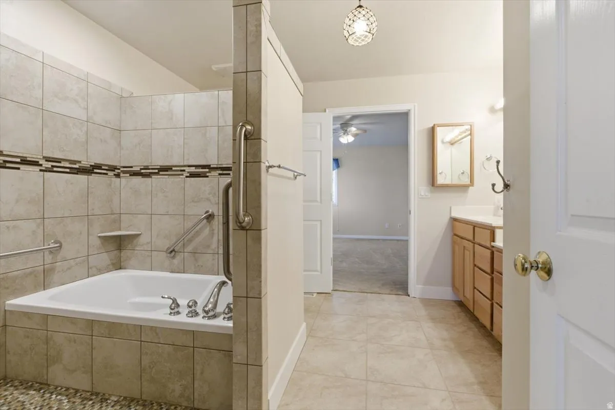 Bathroom featuring vanity, light tile patterned floors, tiled shower, and a garden tub