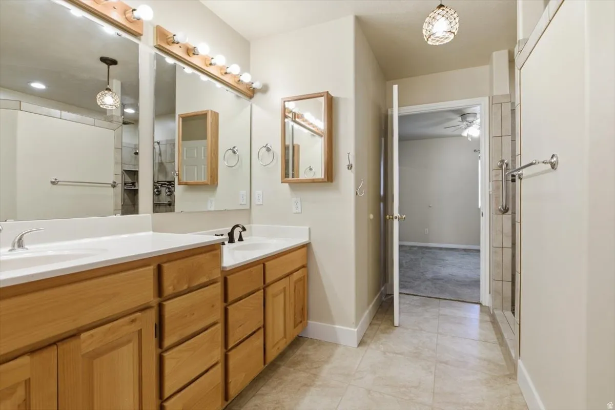 Bathroom featuring double vanity, a shower stall, light tile patterned floors, and a ceiling fan