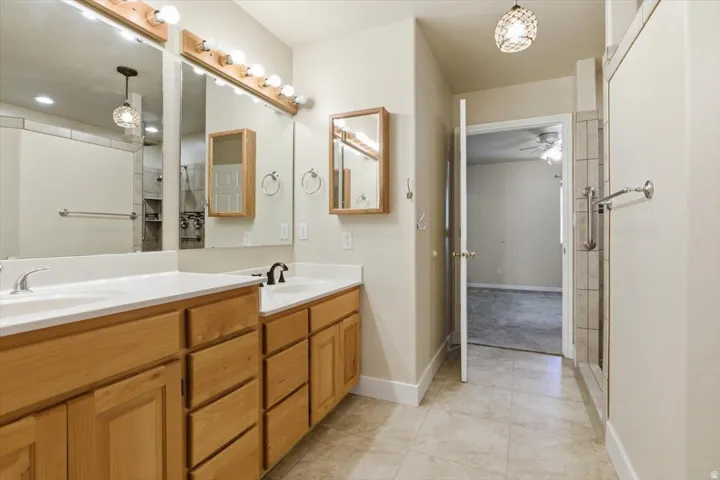 Bathroom featuring double vanity, a shower stall, light tile patterned floors, and a ceiling fan