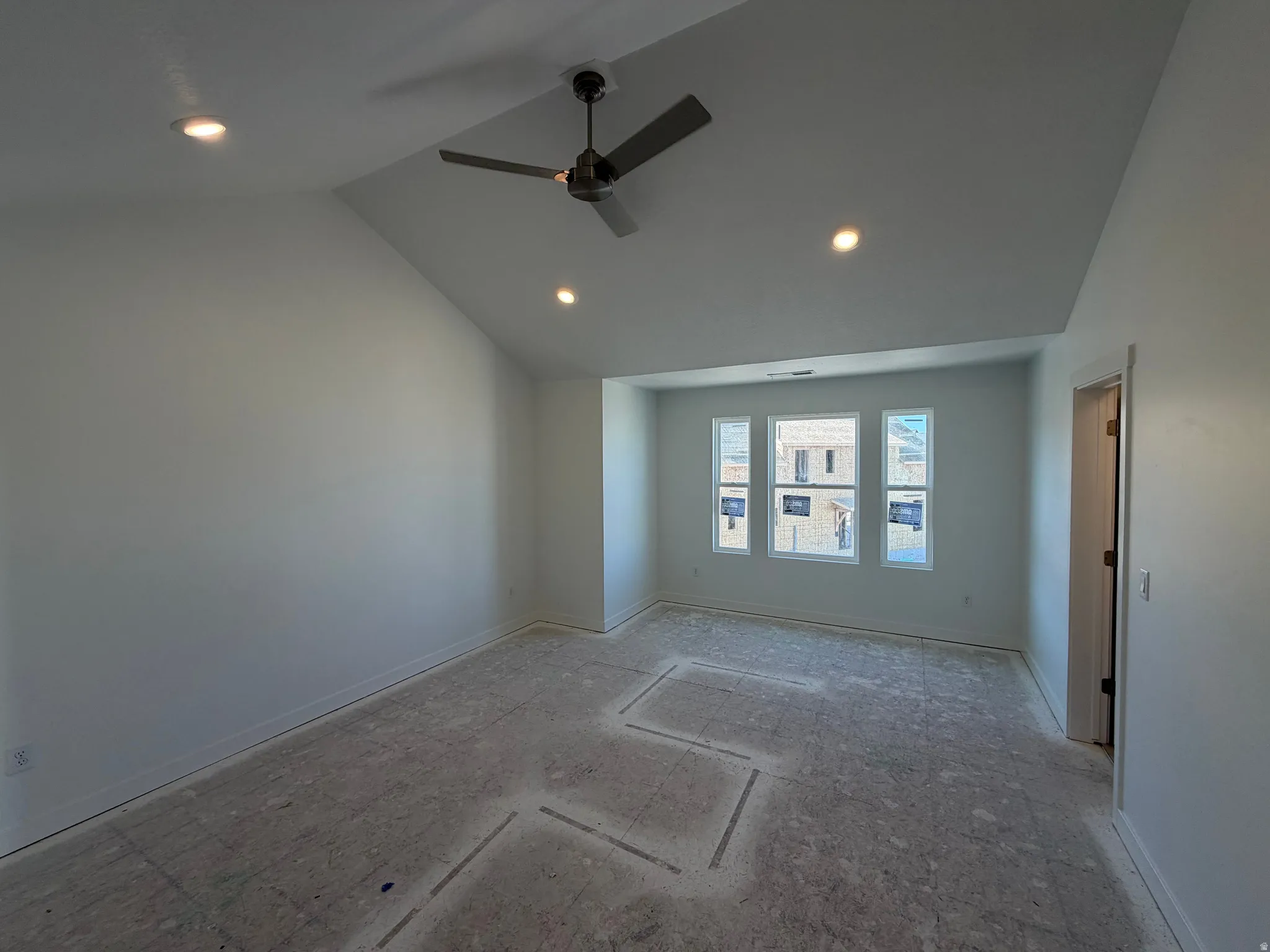 Spacious room featuring a vaulted ceiling with a ceiling fan, recessed lighting, and a series of three windows