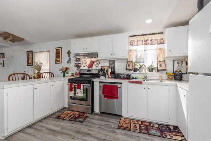 Kitchen with stainless steel appliances, a peninsula, light countertops, white cabinetry, and light wood-style floors