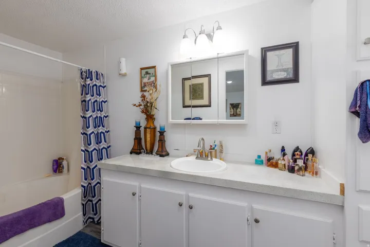 Bathroom with vanity, shower / bath combo with shower curtain, and a textured ceiling