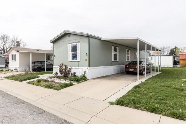 Manufactured / mobile home with an attached carport, concrete driveway, and a front yard