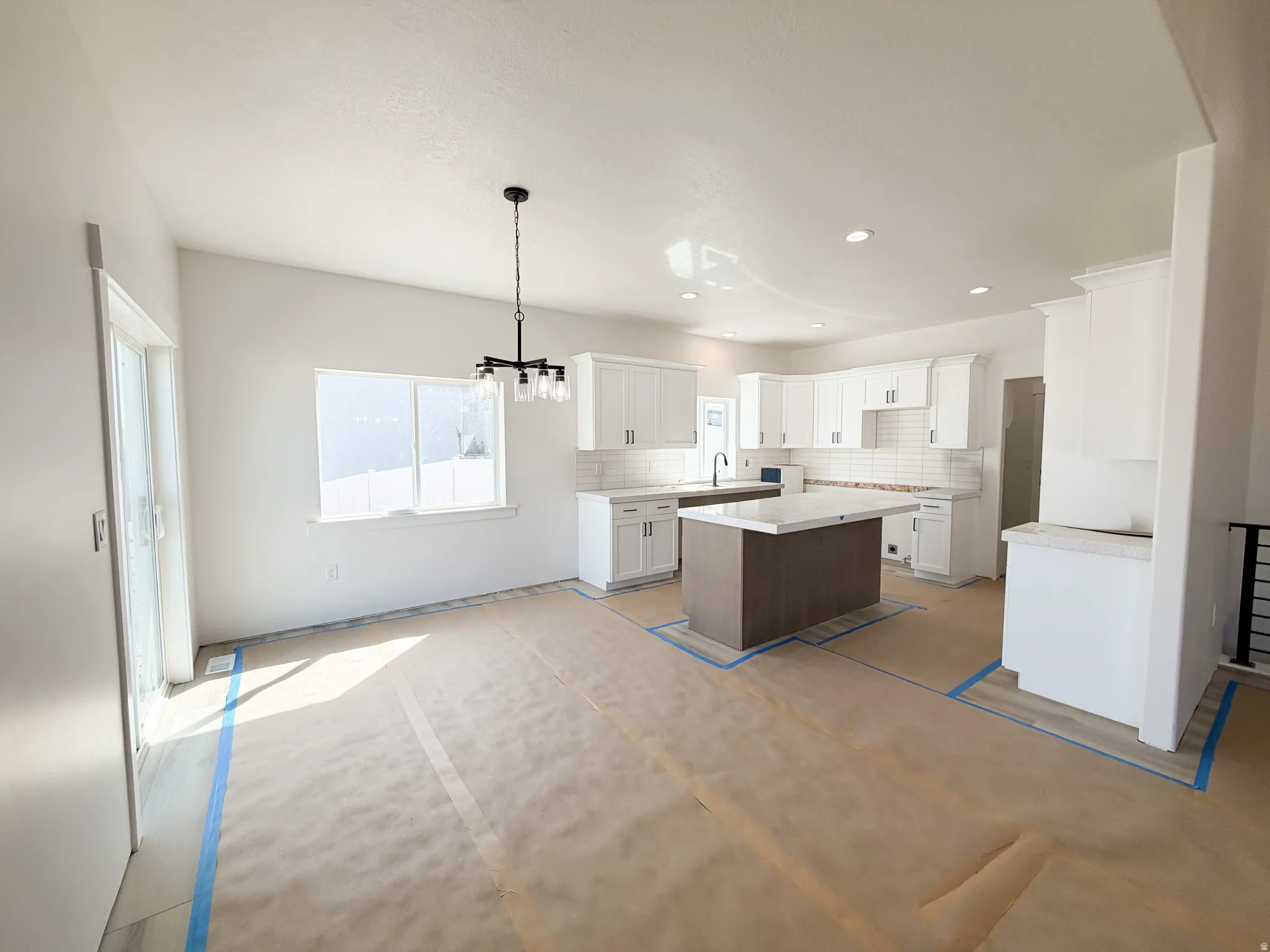 Kitchen with white cabinets, backsplash, a center island, hanging lights, and open floor plan