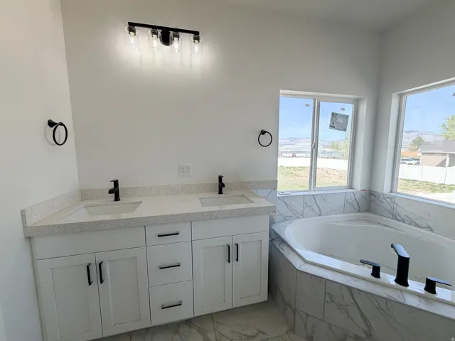Full bathroom featuring double vanity, a garden tub, and light marble finish floors