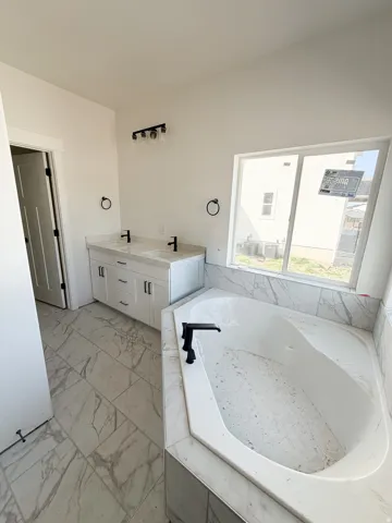 Full bath with double vanity, a bath, and light marble finish floors