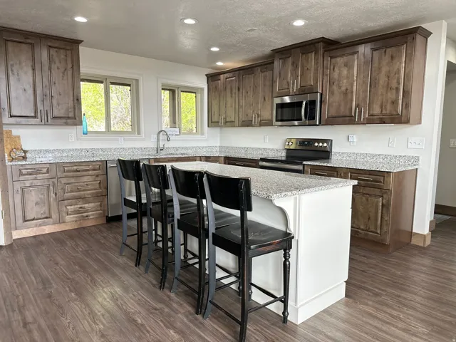 Kitchen with stainless steel appliances, a kitchen breakfast bar, light stone counters, dark wood finished floors, and dark wood finish cabinetry