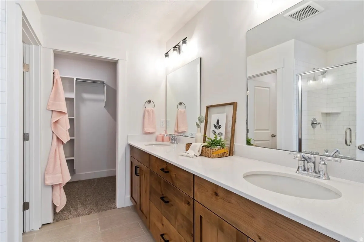 Bathroom with double vanity, a stall shower, and a walk in closet