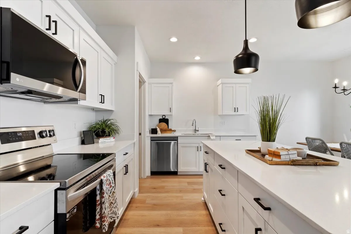 Kitchen featuring stainless steel appliances, pendant lighting, light wood-style floors, white cabinets, and light stone counters