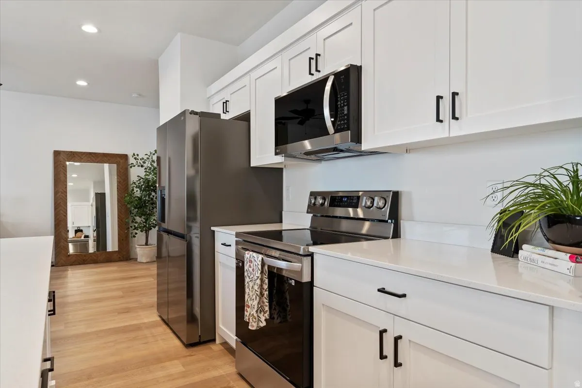 Kitchen featuring stainless steel appliances, recessed lighting, white cabinetry, light wood-style floors, and light stone countertops