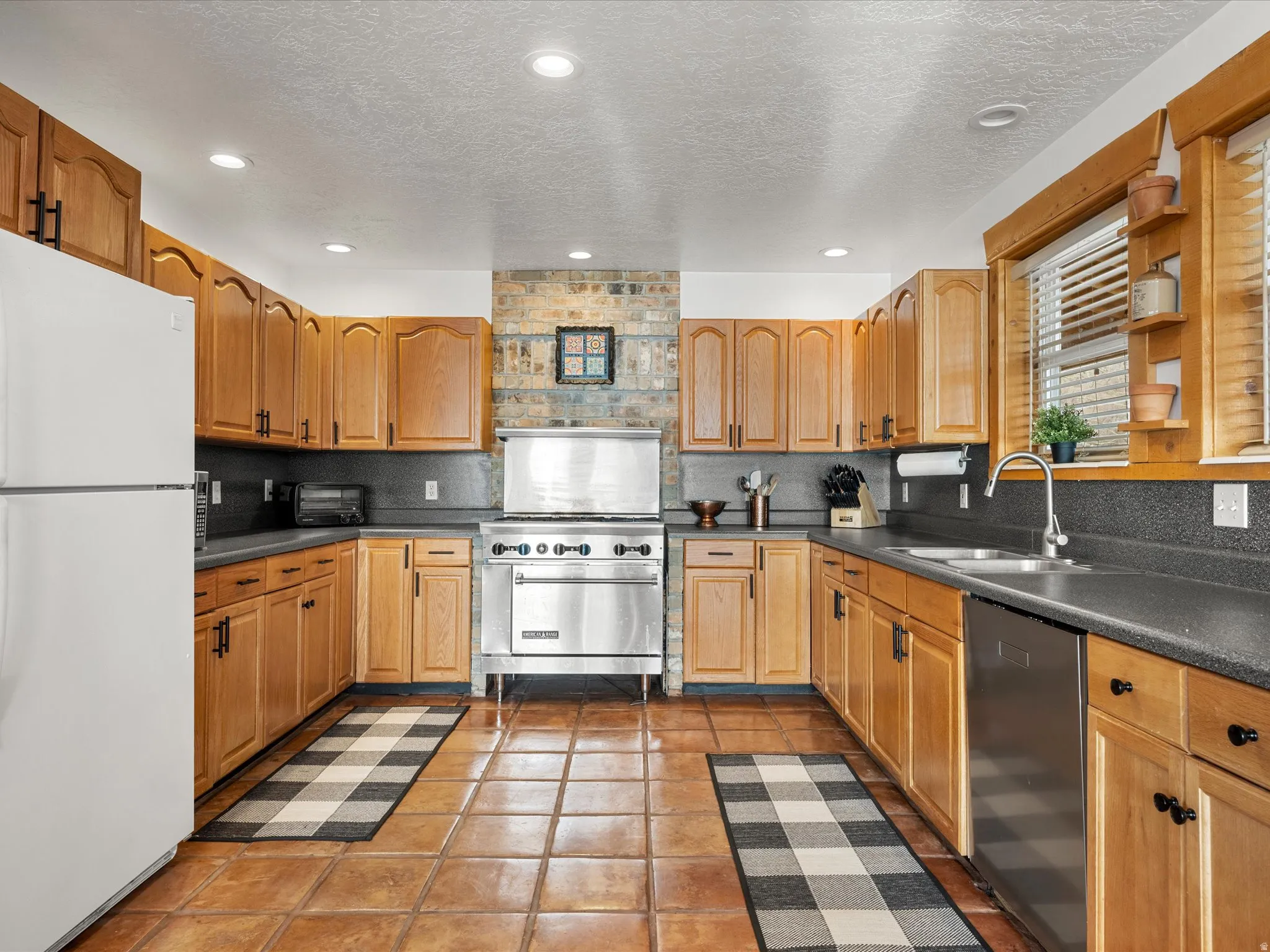 Kitchen with stainless steel appliances, dark countertops, a textured ceiling, light tile patterned floors, and wood finish cabinetry