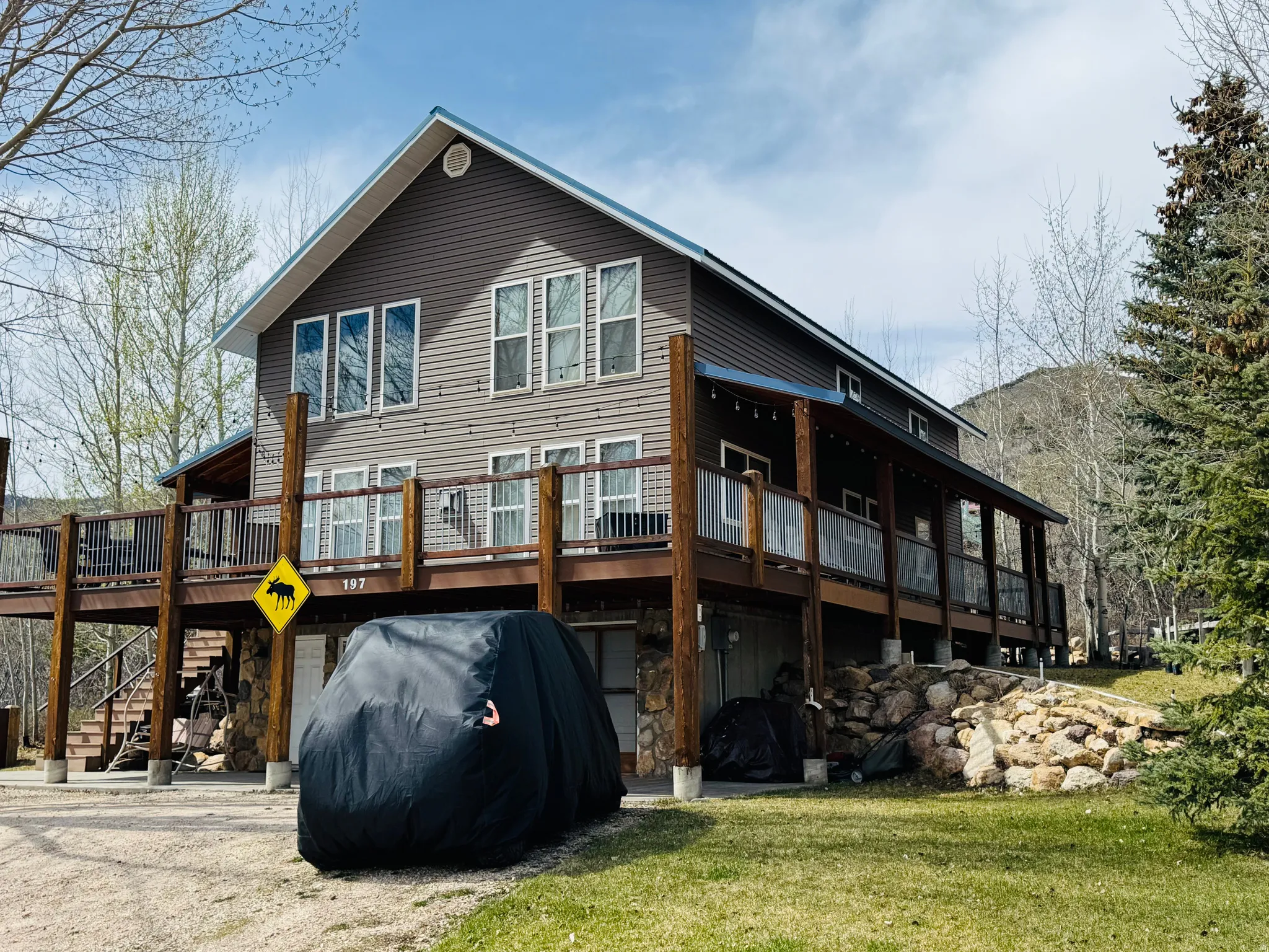 Back of house with a deck, driveway, a garage, stone siding, and a lawn