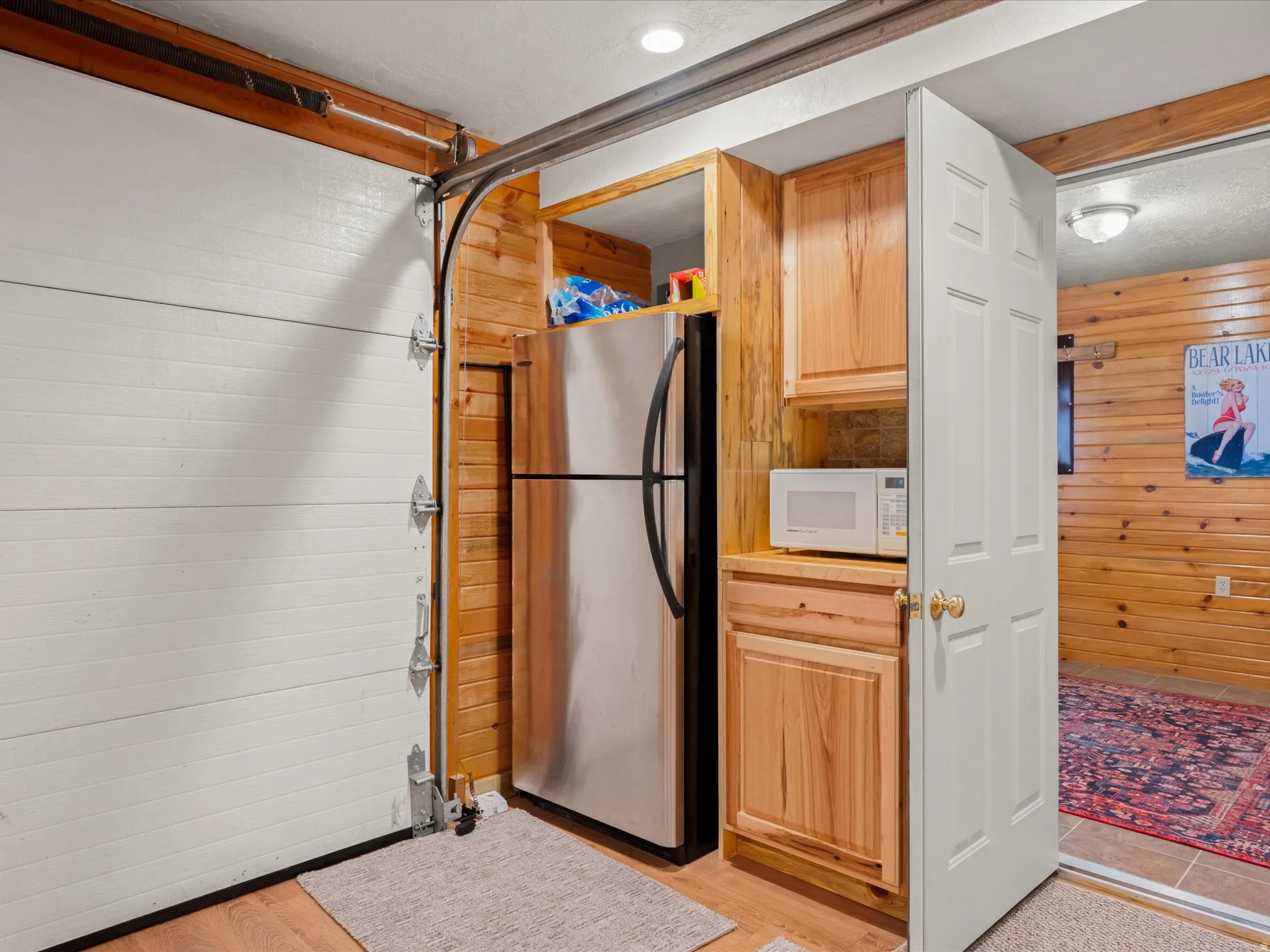 Kitchen featuring wooden walls, freestanding refrigerator, white microwave, light countertops, and light wood finish cabinetry