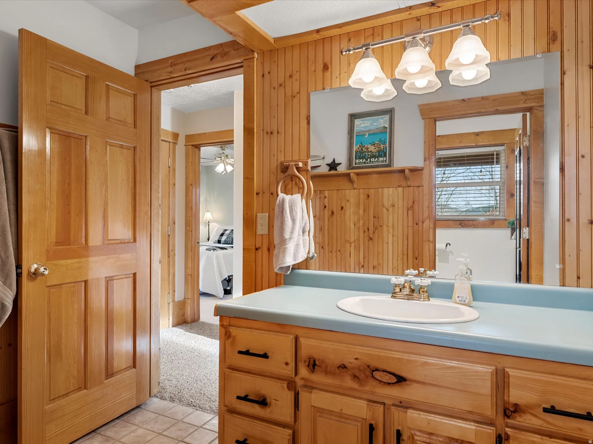 Ensuite bathroom featuring vanity, light tile patterned floors, a ceiling fan, light carpet, and wood walls