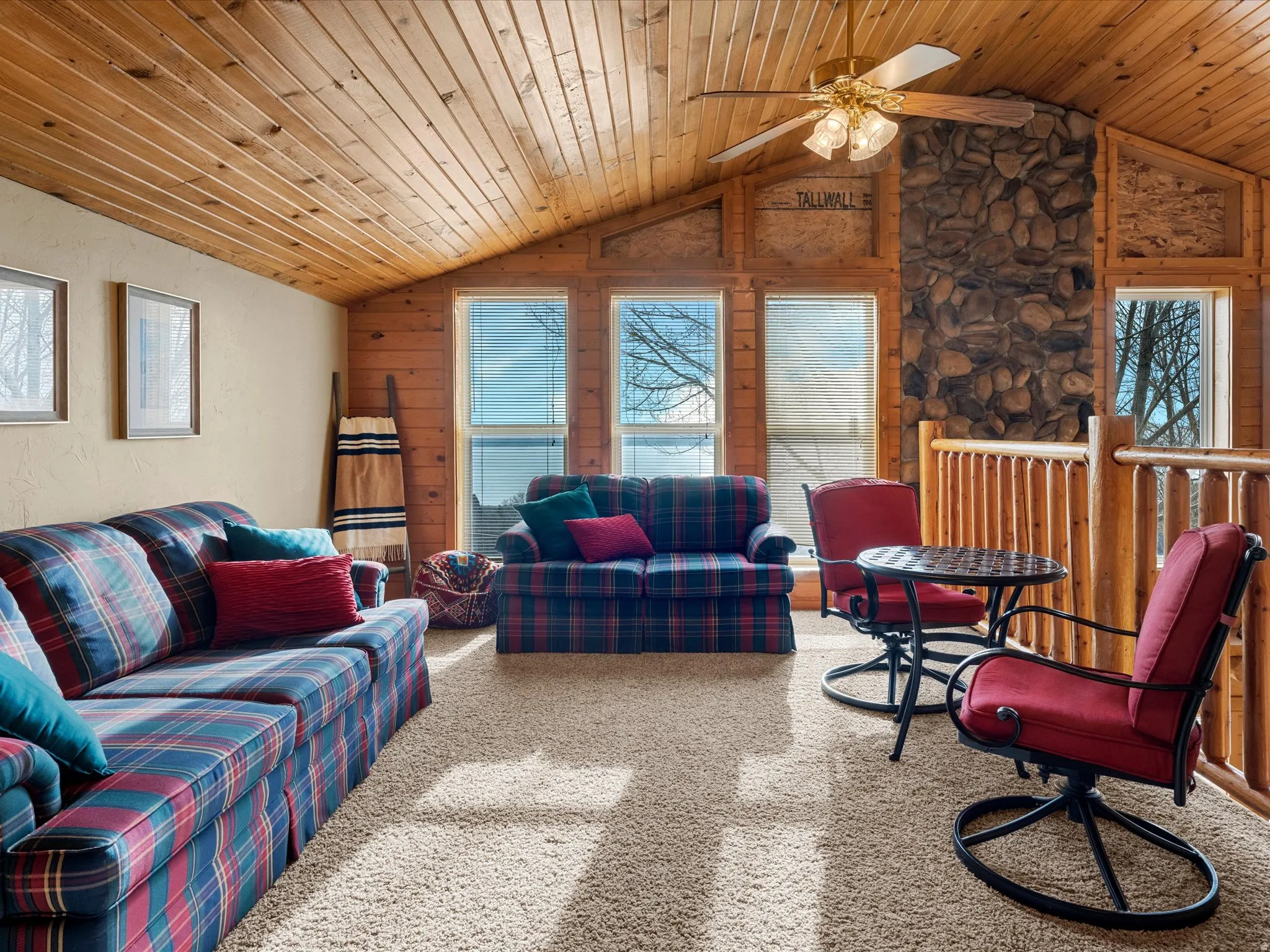 Carpeted living area with a ceiling fan, wooden ceiling, and wooden walls