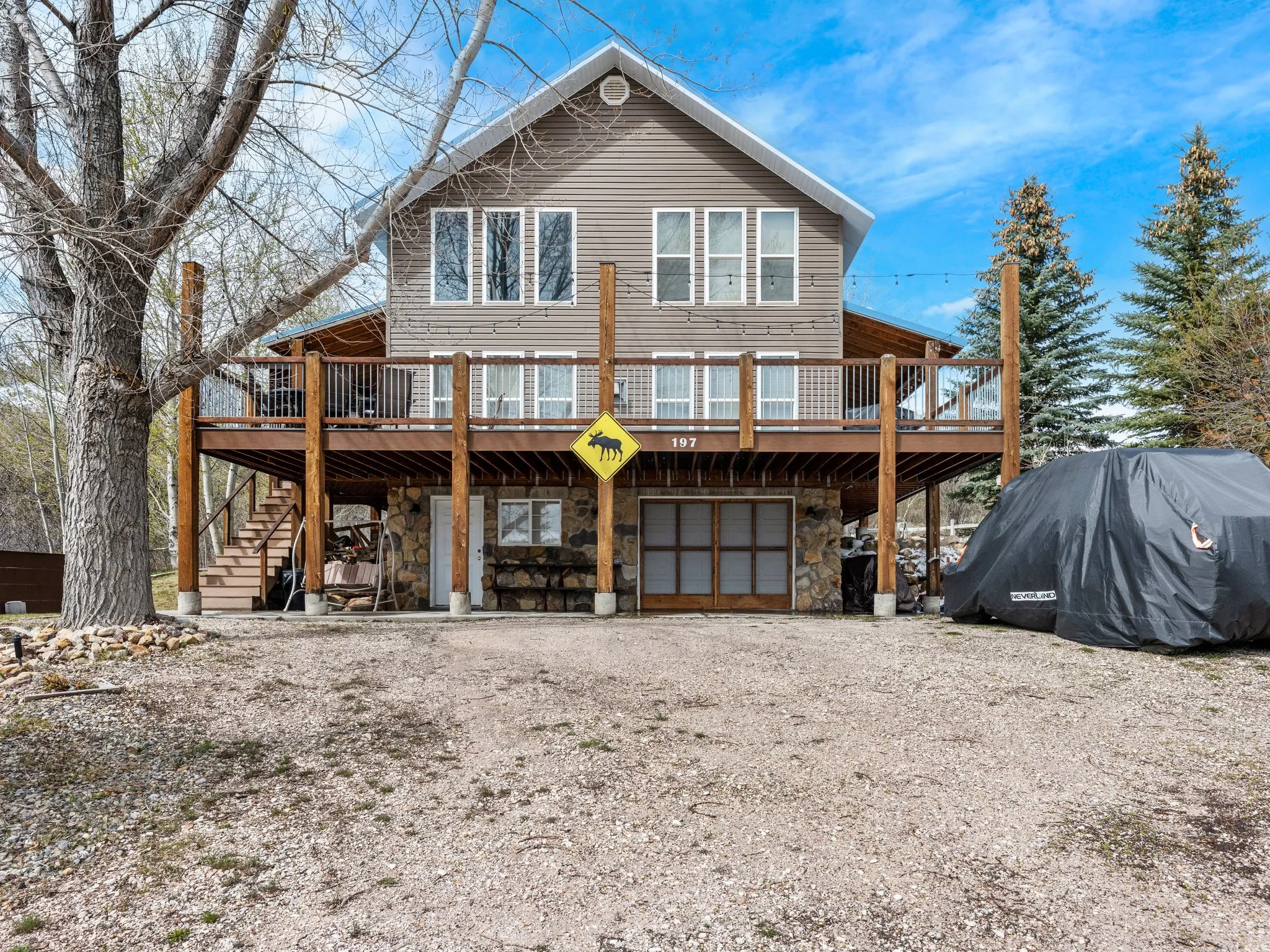 Back of property with a deck, stone siding, driveway, and a garage