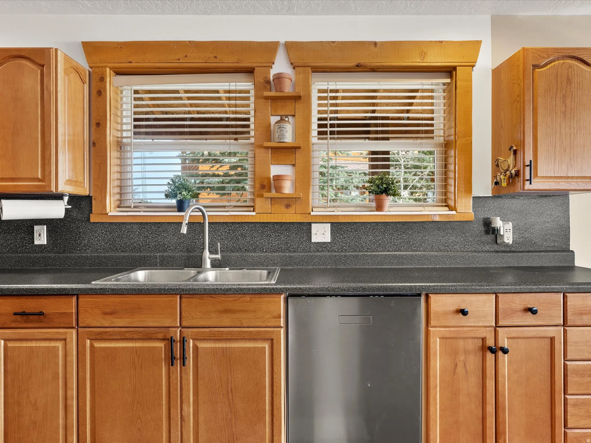 Kitchen featuring stainless steel dishwasher, dark countertops, backsplash, and wood finish cabinetry