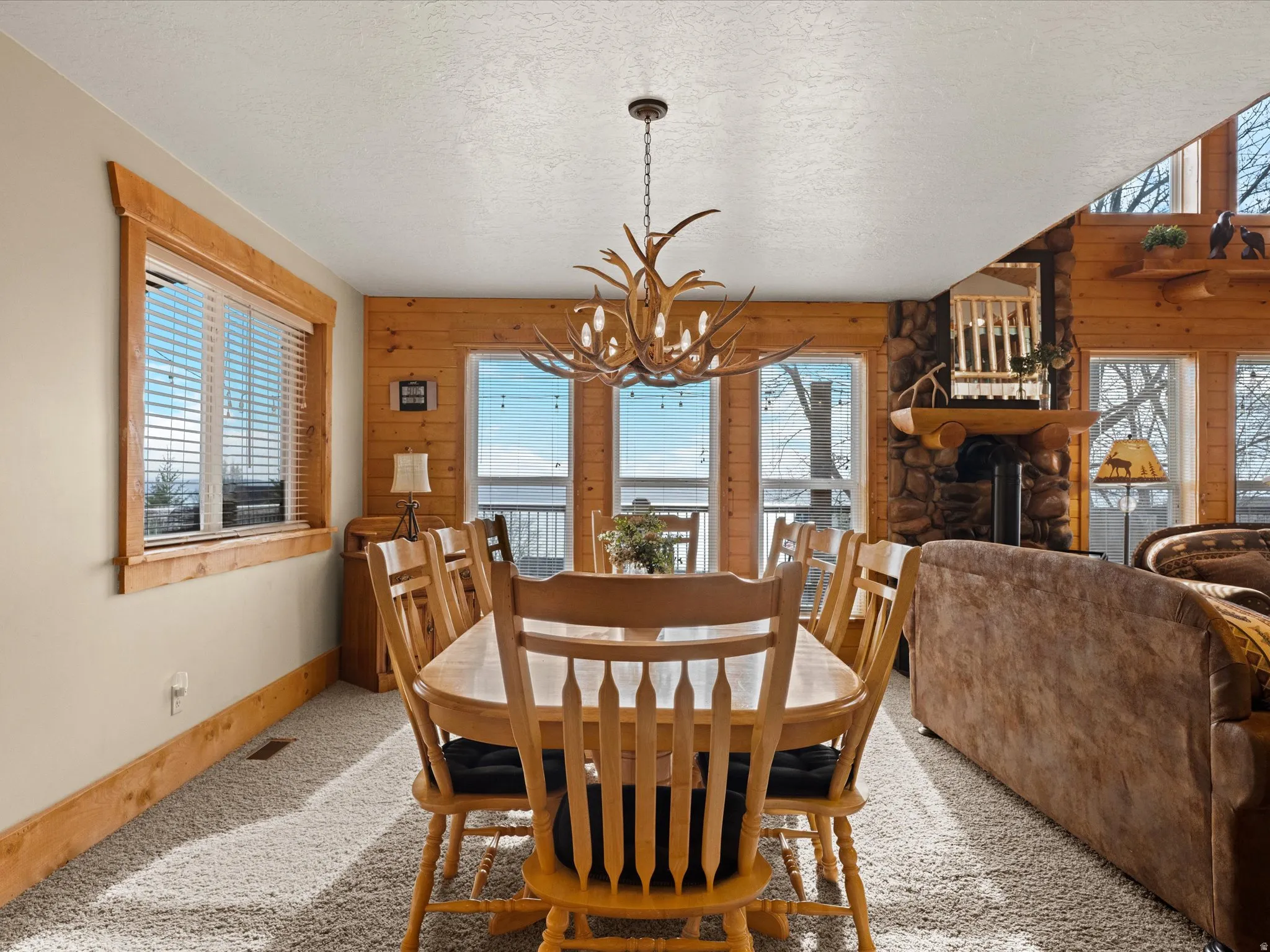 Dining room with carpet floors, suspended lighting, a fireplace, wooden walls, and a textured ceiling