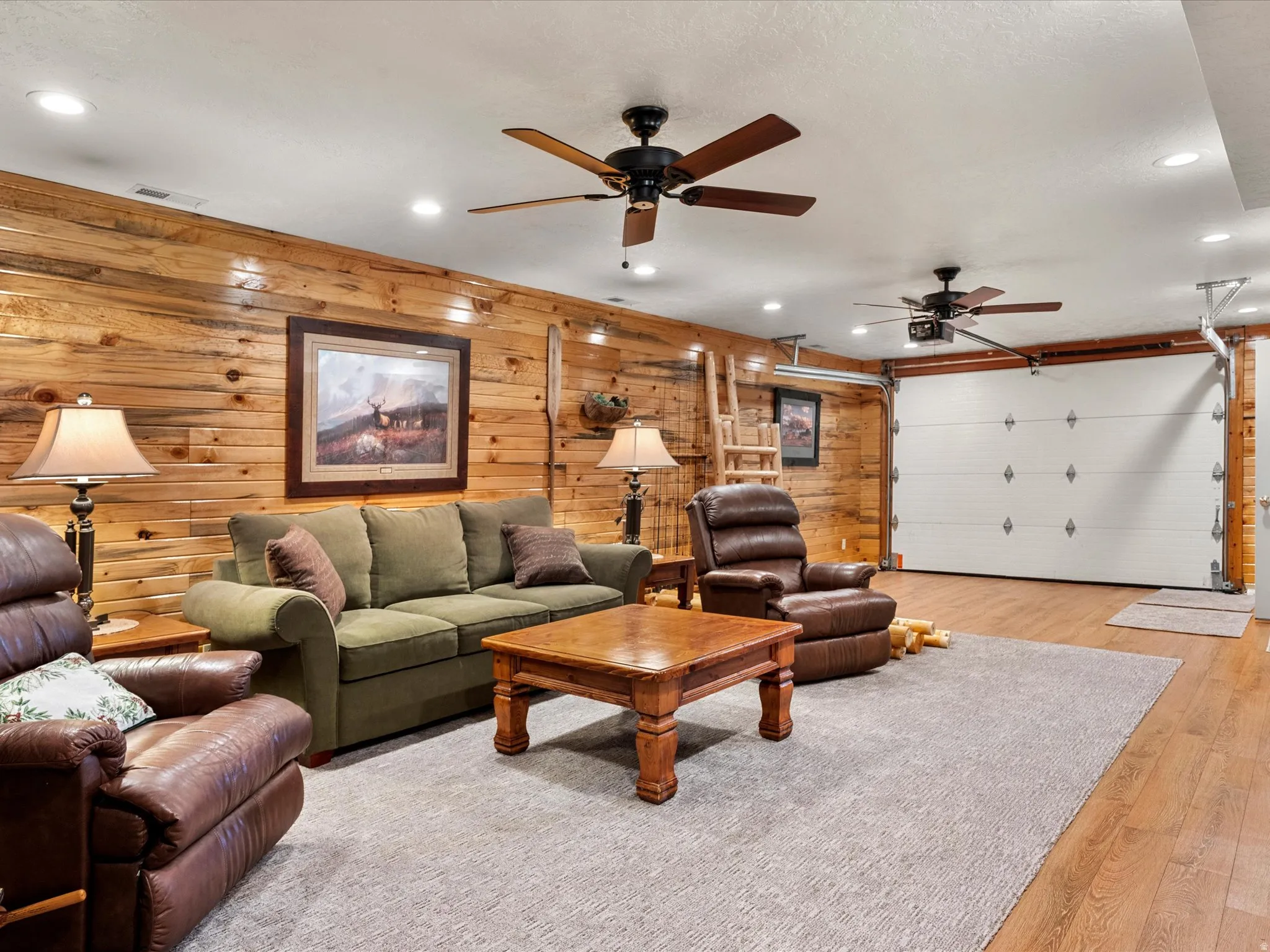 Living area with recessed lighting, ceiling fan, wood finished floors, wood walls, and a garage