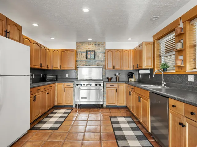 Kitchen with stainless steel appliances, dark countertops, a textured ceiling, light tile patterned floors, and wood finish cabinetry