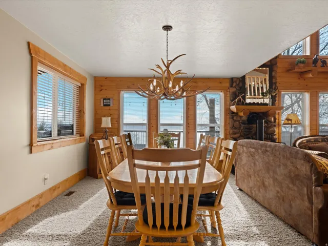 Dining room with carpet floors, suspended lighting, a fireplace, wooden walls, and a textured ceiling
