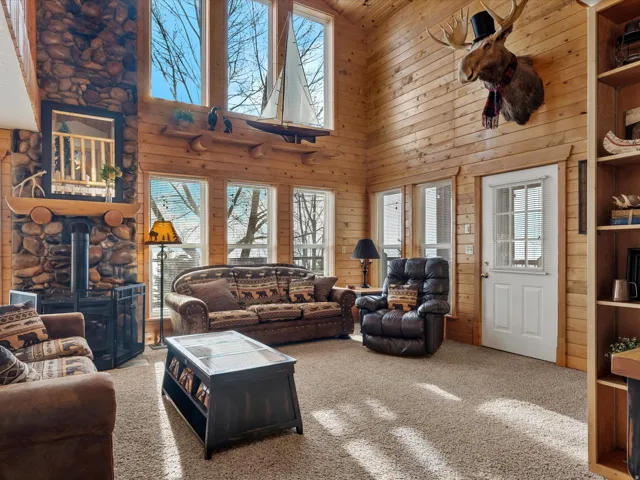 Carpeted living room with a wood stove, a high ceiling, and wooden walls
