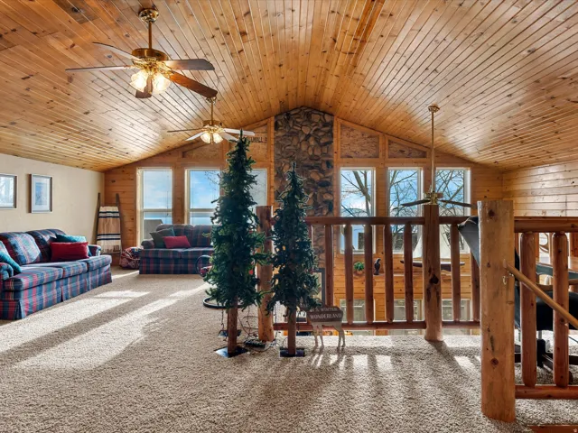 Carpeted living room featuring a ceiling fan, wooden walls, and wood ceiling
