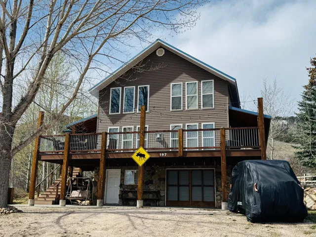 Back of property featuring a deck, a garage, driveway, and stone siding