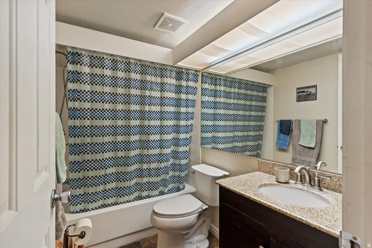 Full bathroom with vanity, shower / bath combo, and a textured ceiling