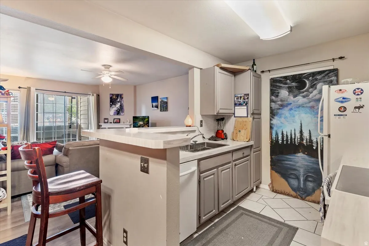 Kitchen featuring white appliances, gray cabinets, light countertops, ceiling fan, and a peninsula