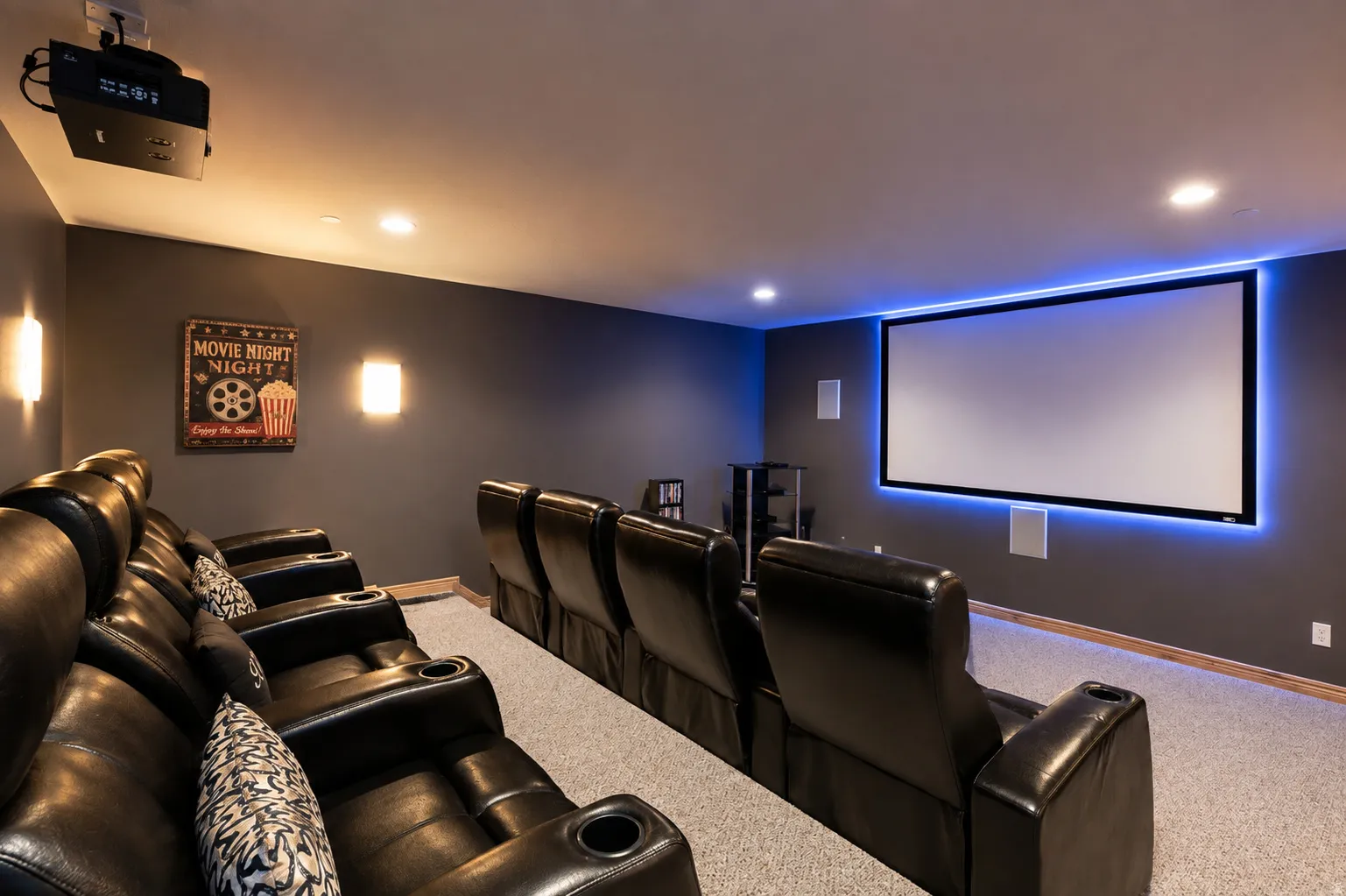 Dedicated media room featuring a large projection screen with integrated backlighting, recessed ceiling lighting, and wall sconces