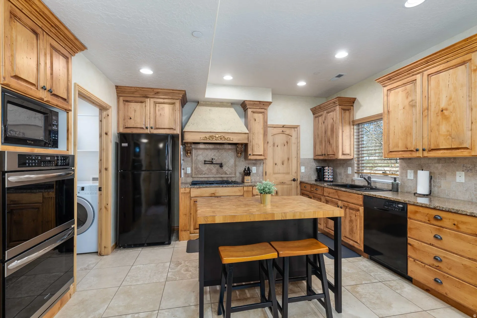 Kitchen with black appliances, light stone countertops, washer / clothes dryer, decorative backsplash, and light tile patterned flooring