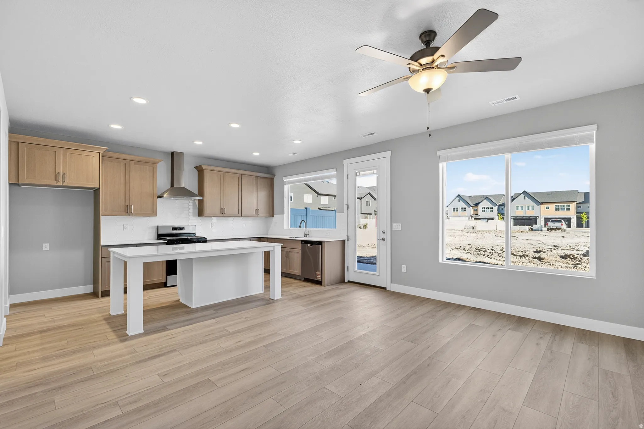 Kitchen featuring stainless steel appliances, a kitchen island, a ceiling fan, light wood-style flooring, and a kitchen bar
