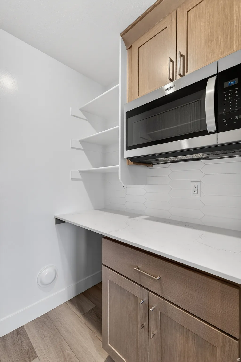 Kitchen view of stainless steel microwave, light wood finished floors, light stone countertops, light wood finish cabinets, and decorative backsplash