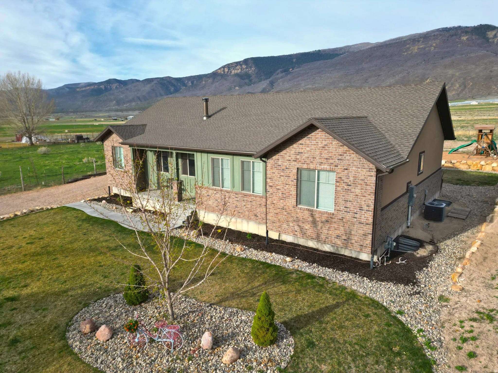 Rear view of house with roof with shingles, brick siding, a mountain view, and a yard