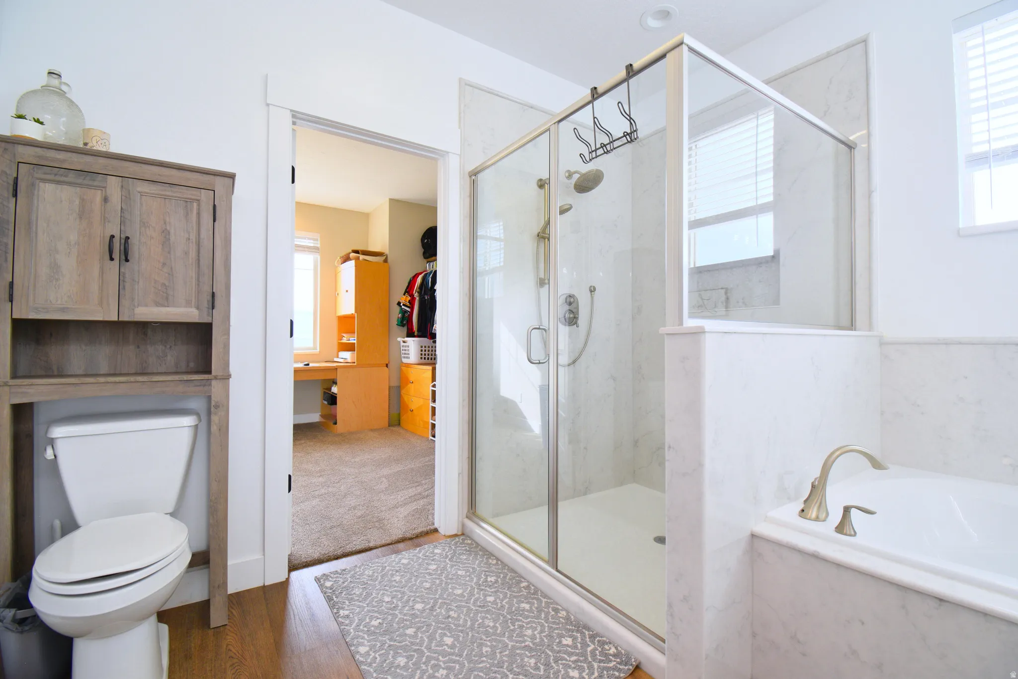 Bathroom with a marble finish shower, a bath, a walk in closet, and dark wood-style floors