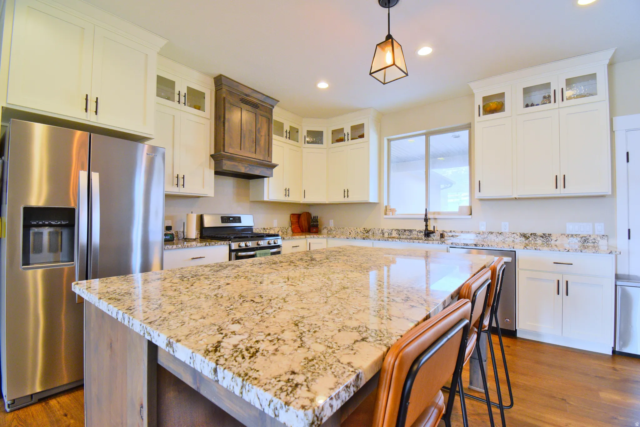 Kitchen featuring stainless steel appliances, glass fronted cabinets, a kitchen island, light stone counters, and pendant lighting