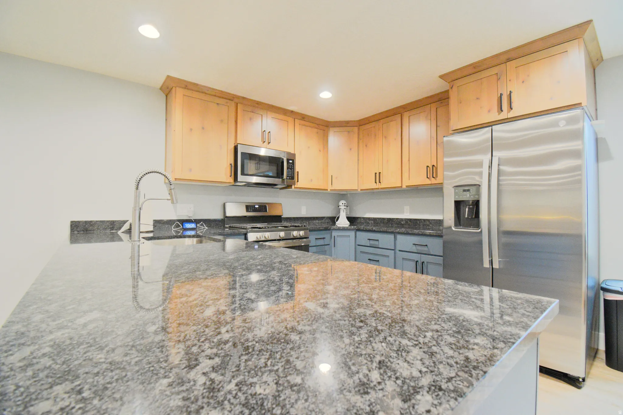 Kitchen featuring stainless steel appliances, dark stone counters, light wood finish cabinets, recessed lighting, and a peninsula