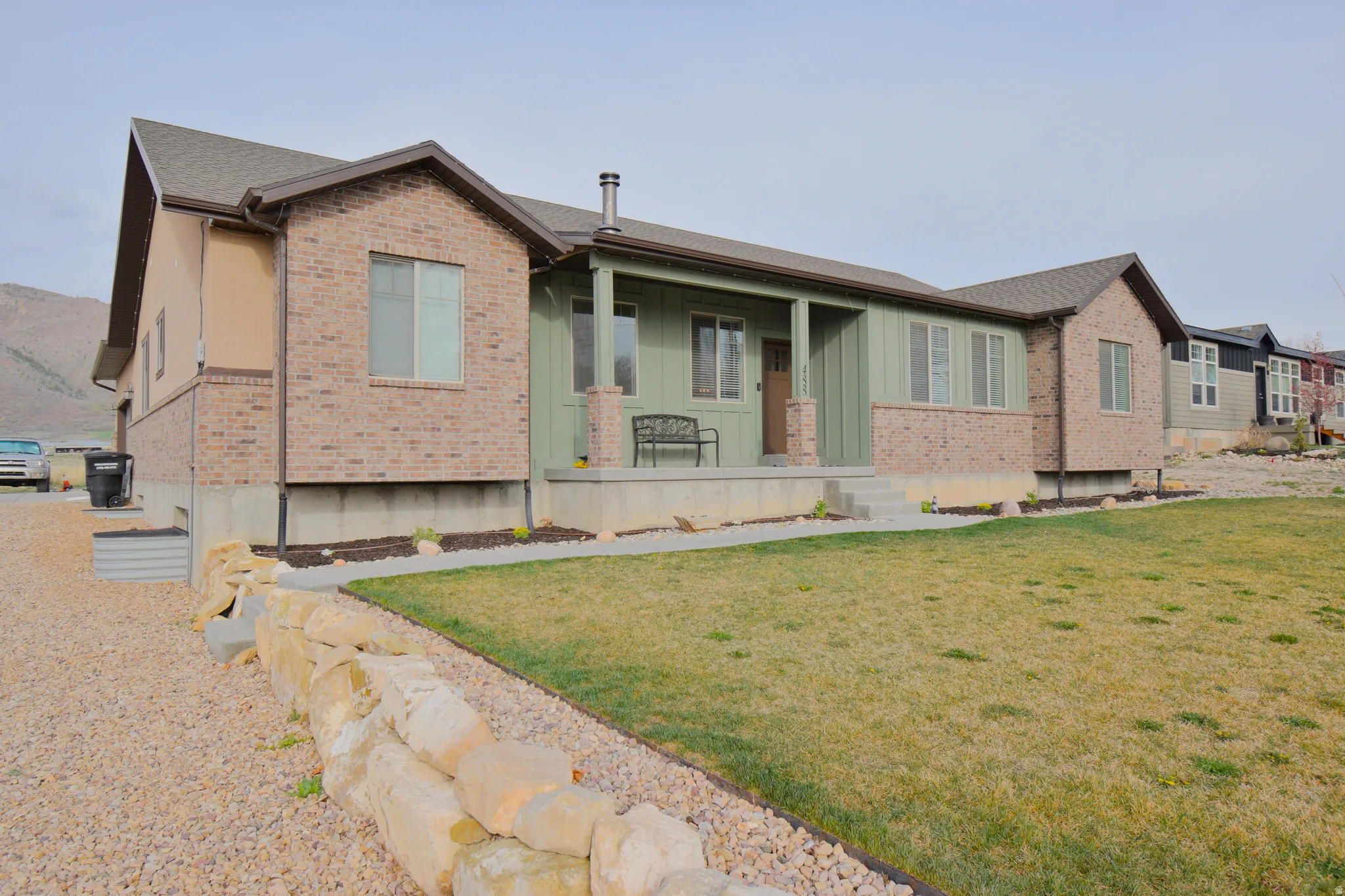 View of front facade with a porch, brick siding, a front yard, and board and batten siding