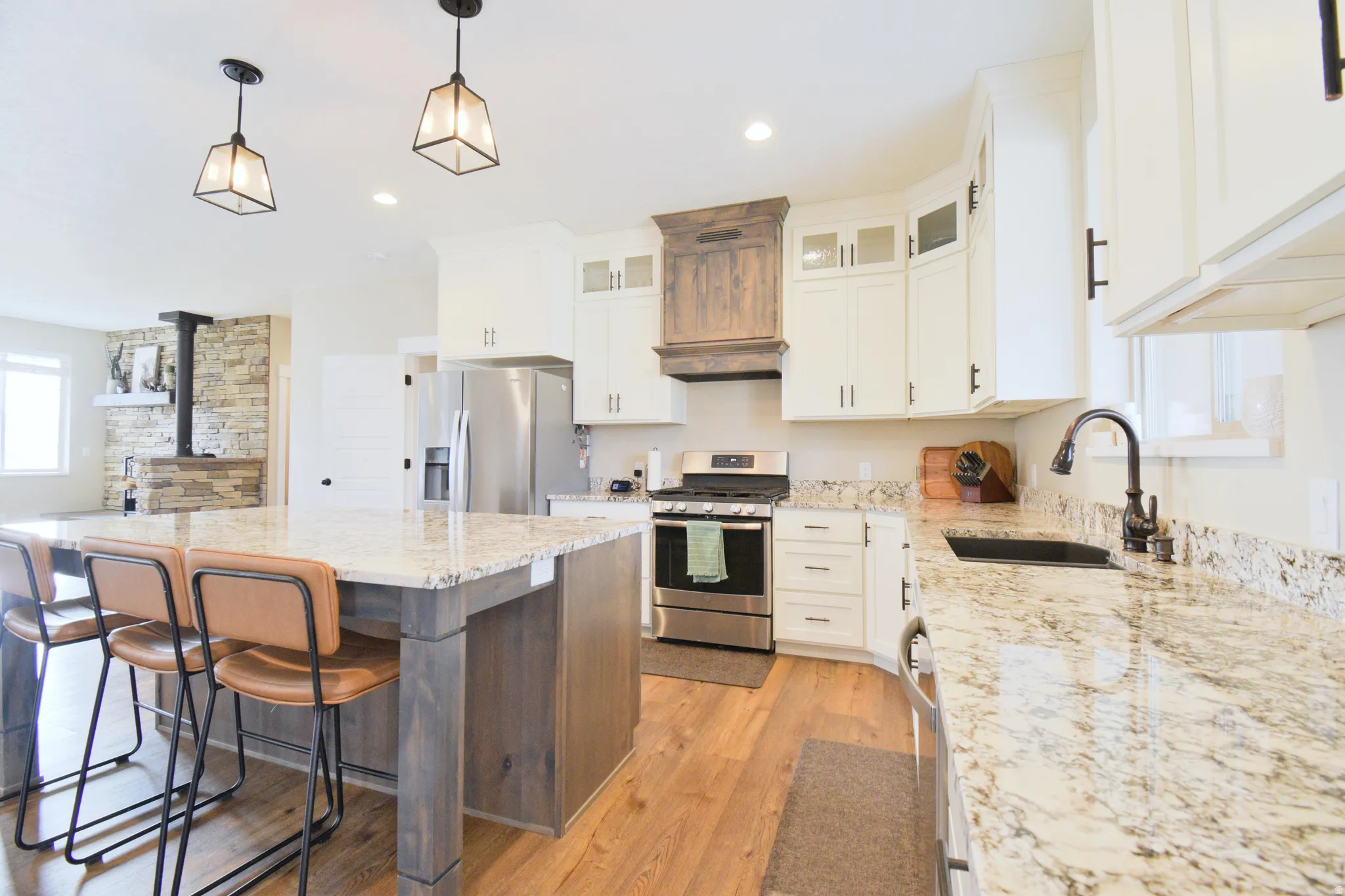 Dual tone kitchen with stainless steel appliances, light wood-style floors, dual tone cabinets, light stone countertops, and glass fronted cabinets