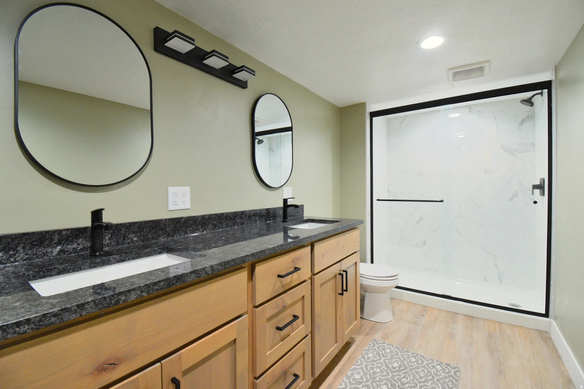 Bathroom with double vanity, a marble finish shower, light wood finished floors, and recessed lighting
