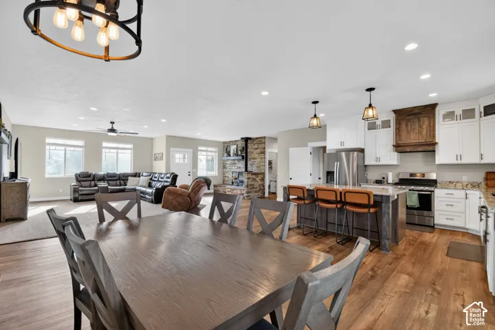 Open-concept living space featuring wood-finish flooring, a kitchen island with pendant lighting, white cabinetry, stainless steel appliances, and a stone-clad fireplace