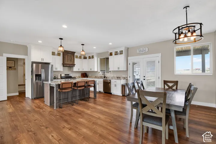 Open-concept kitchen and dining area featuring wood-finish flooring, a kitchen island with seating, stainless steel appliances, white cabinetry, and double glass-paneled doors