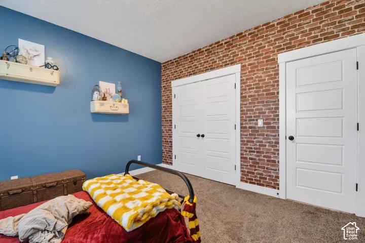 Bedroom featuring an exposed brick accent wall, white paneled doors, and plush carpet flooring