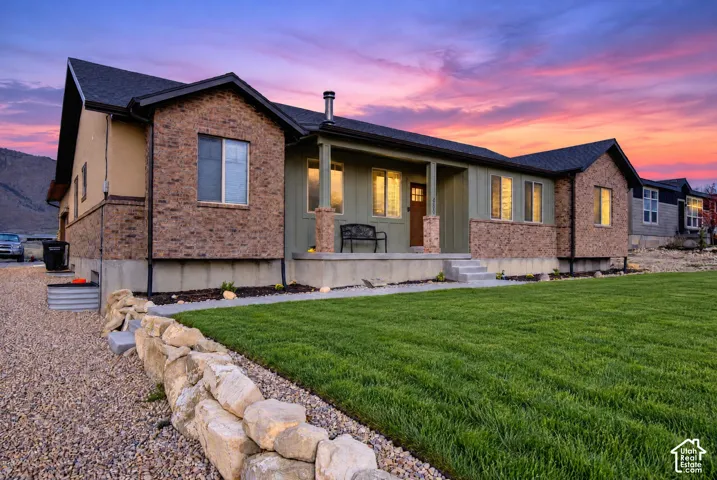 Exterior featuring a combination of brick and vertical siding, a covered front porch with stone-base columns, a concrete walkway, and a tiered rock retaining wall