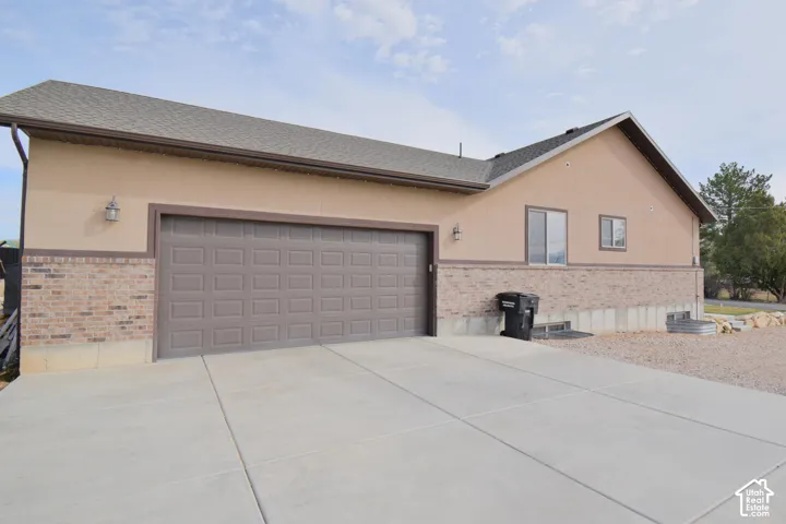 View of property exterior featuring stucco siding, brick siding, driveway, and a garage