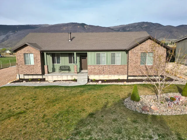 Single story home with covered porch, a mountain view, brick siding, a shingled roof, and a front yard